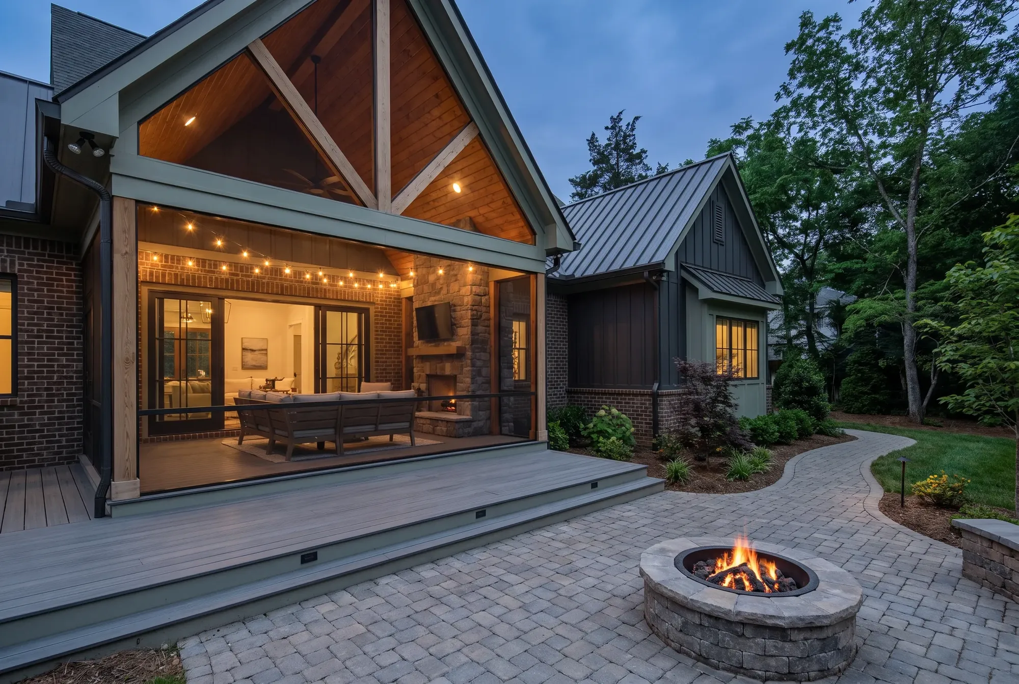 Screened porch with a stained cathedral ceiling and stone fireplace opening onto a composite deck and paver patio at dusk