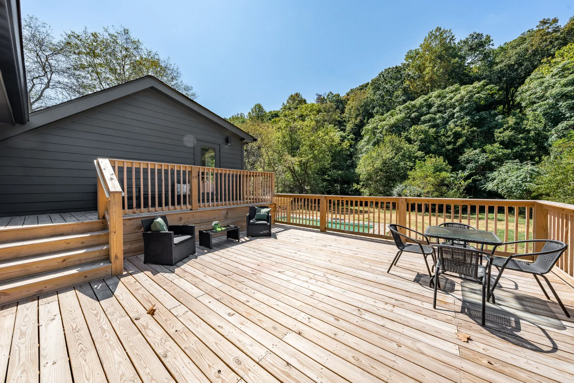 New pressure-treated deck with stairs and a dining set behind a renovated dark gray ranch home in Middle Tennessee