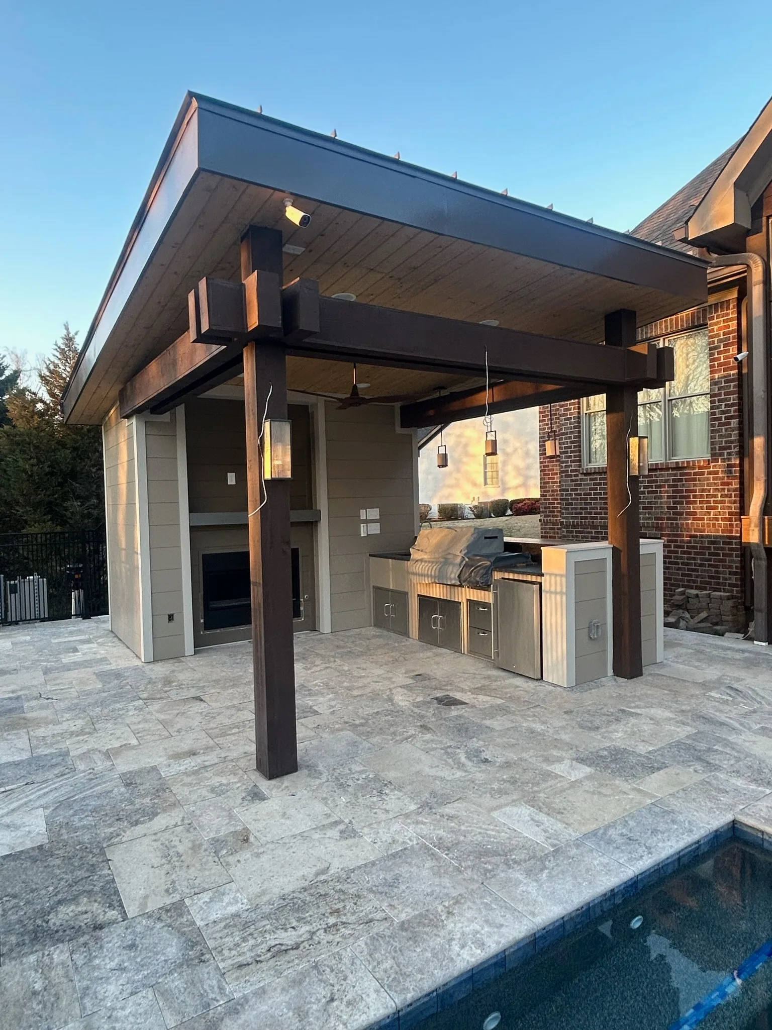 Tall covered patio structure beside a pool with outdoor kitchen and ceiling fans
