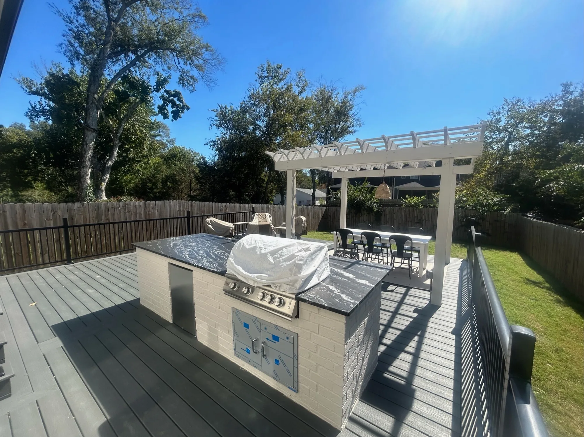 Composite deck with a tiled outdoor kitchen island and a white pergola