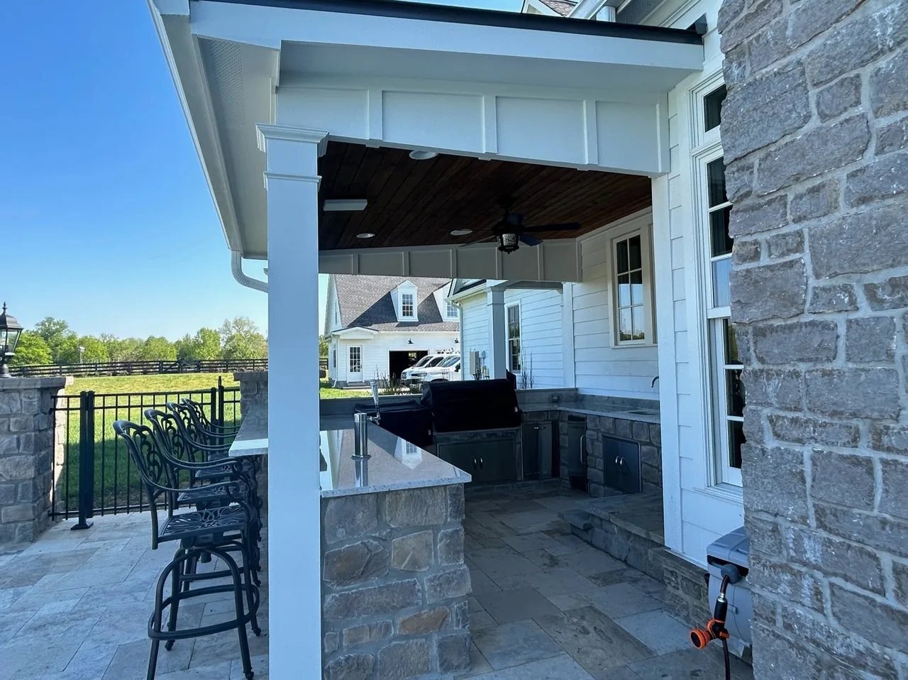 Covered back porch with a stone outdoor kitchen island and bar seating on a farmhouse-style home