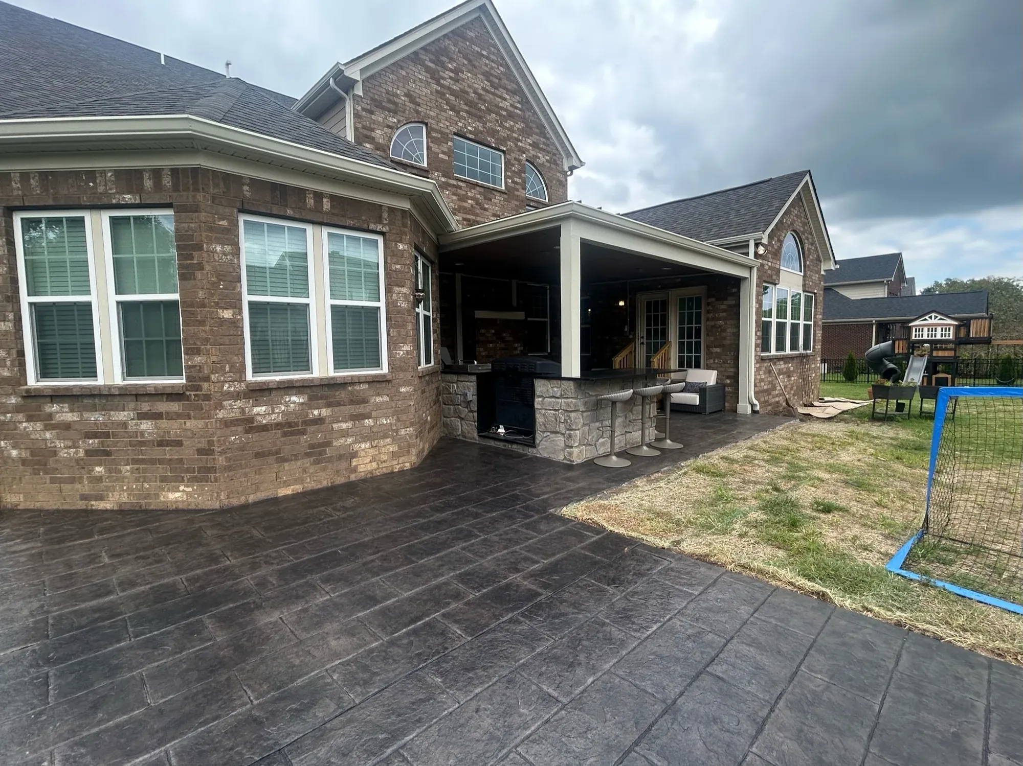 Rear of a brick home with a covered porch and a new stamped concrete patio