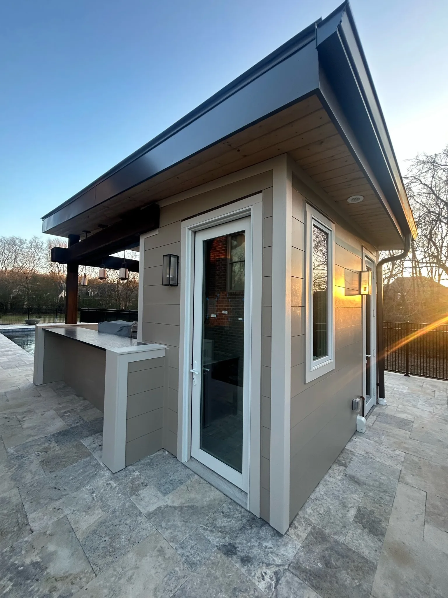 Small pool house with travertine patio at sunset, built as part of an outdoor living project