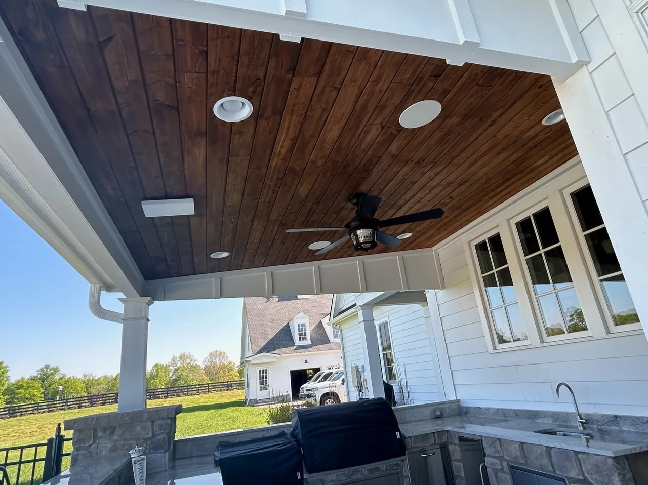 Covered porch with a stained tongue-and-groove ceiling, recessed lighting and an outdoor kitchen built by Southern Belle Construction